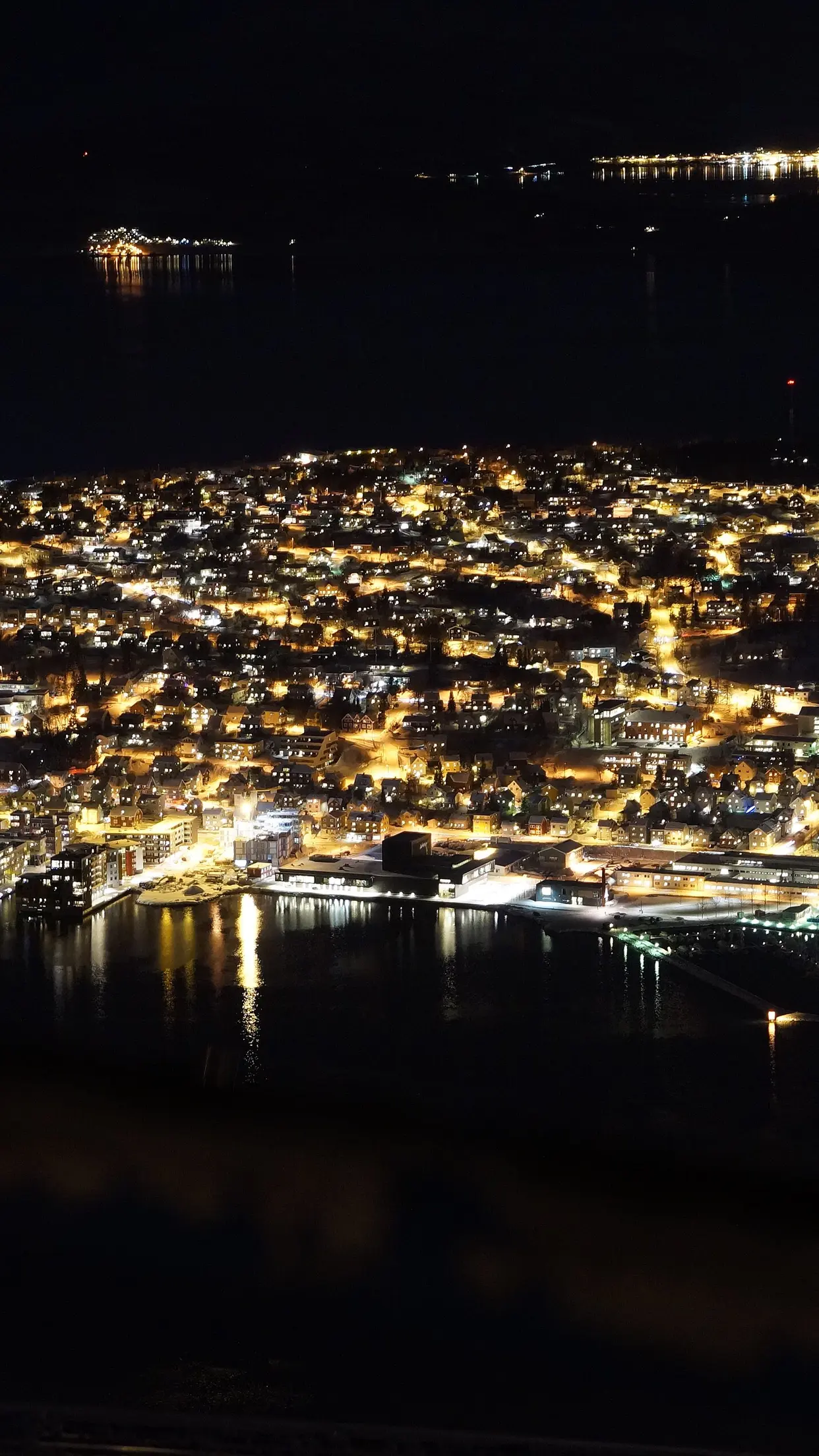 Tromsø acesa à noite, vista do alto, sobre o mar escuro.
