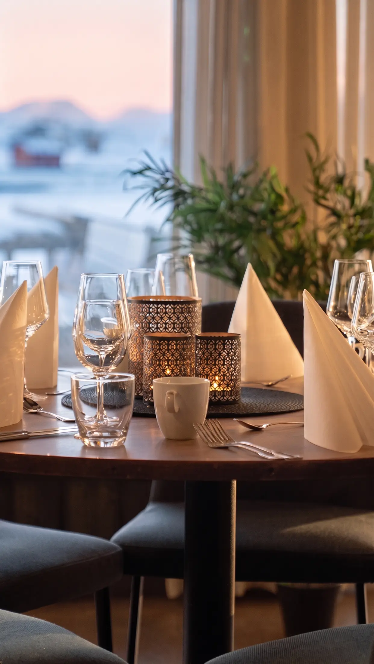 Mesa posta no restaurante do Sommarøy Arctic Hotel, com velas acesas e o céu claro do meio-dia de inverno na janela.