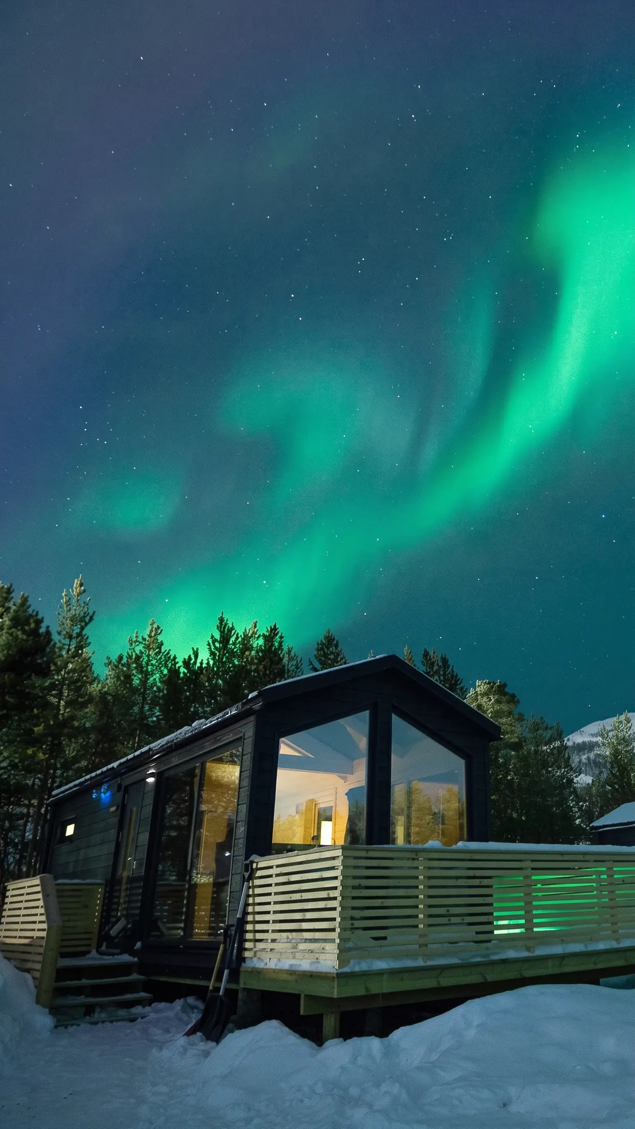 O chalé de vidro aceso na floresta, com a aurora acima.