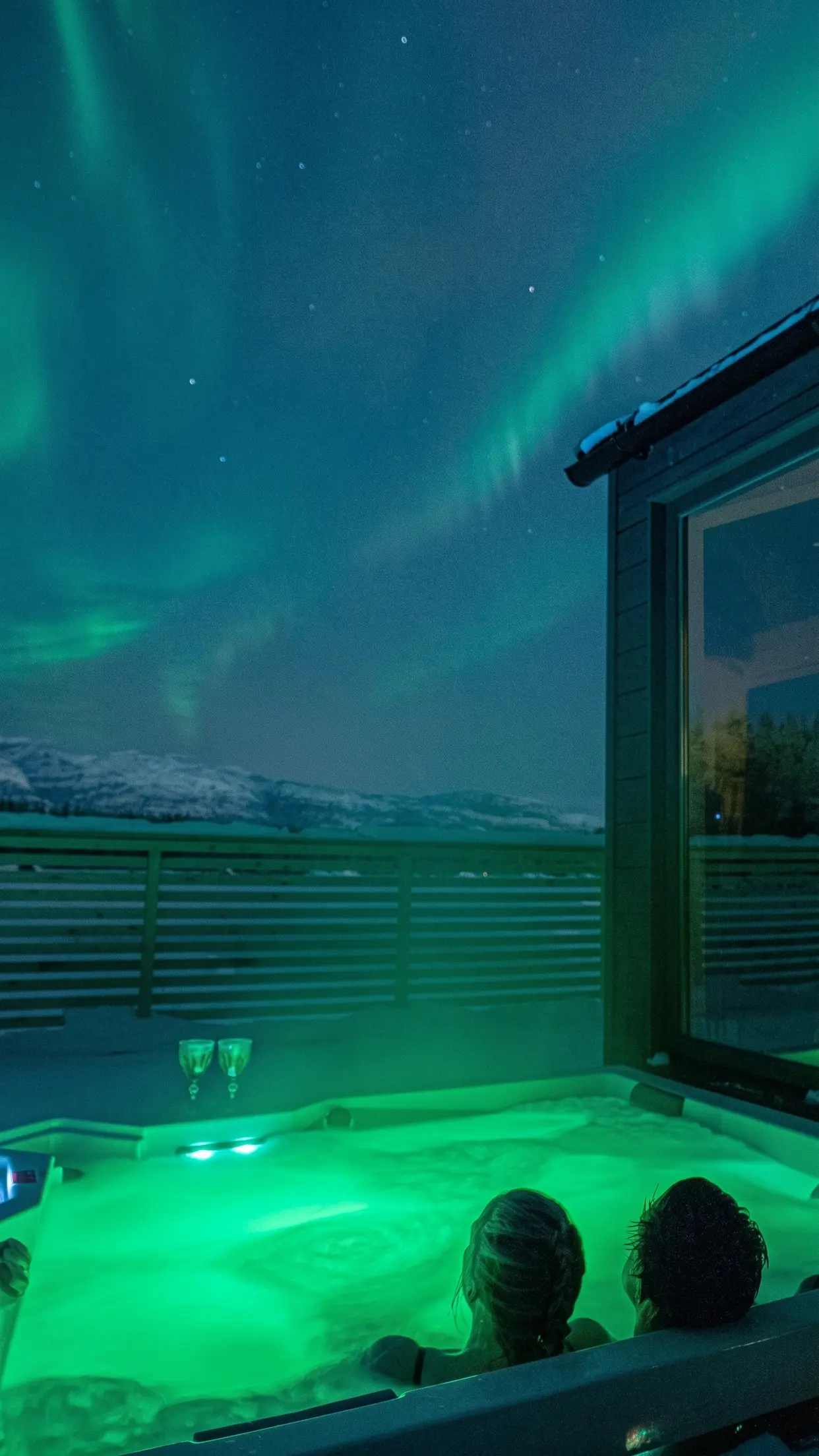 Jacuzzi no deck do chalé de vidro, sob a aurora.